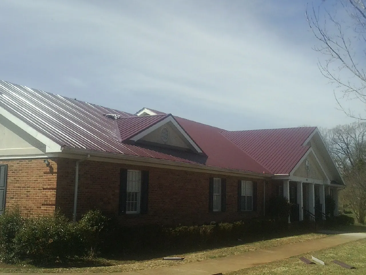 Red metal roof with gabled entries on a long brick building, from a Hail Damage Roof Repair job in Nanticoke