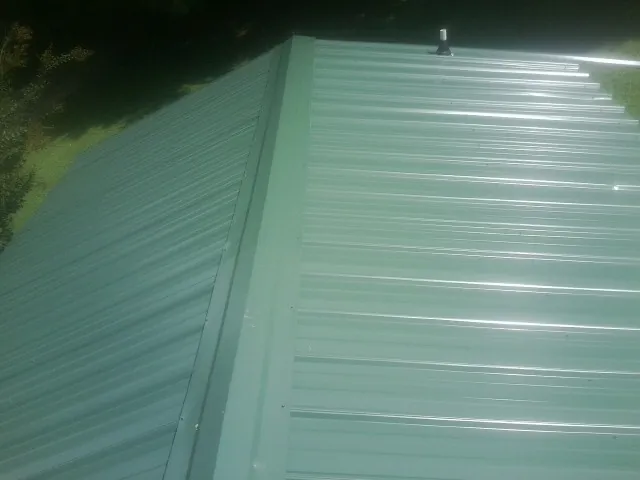 New green metal panels meeting at the ridge of a roof — Flat Roof Repair work by our crew in Nanticoke