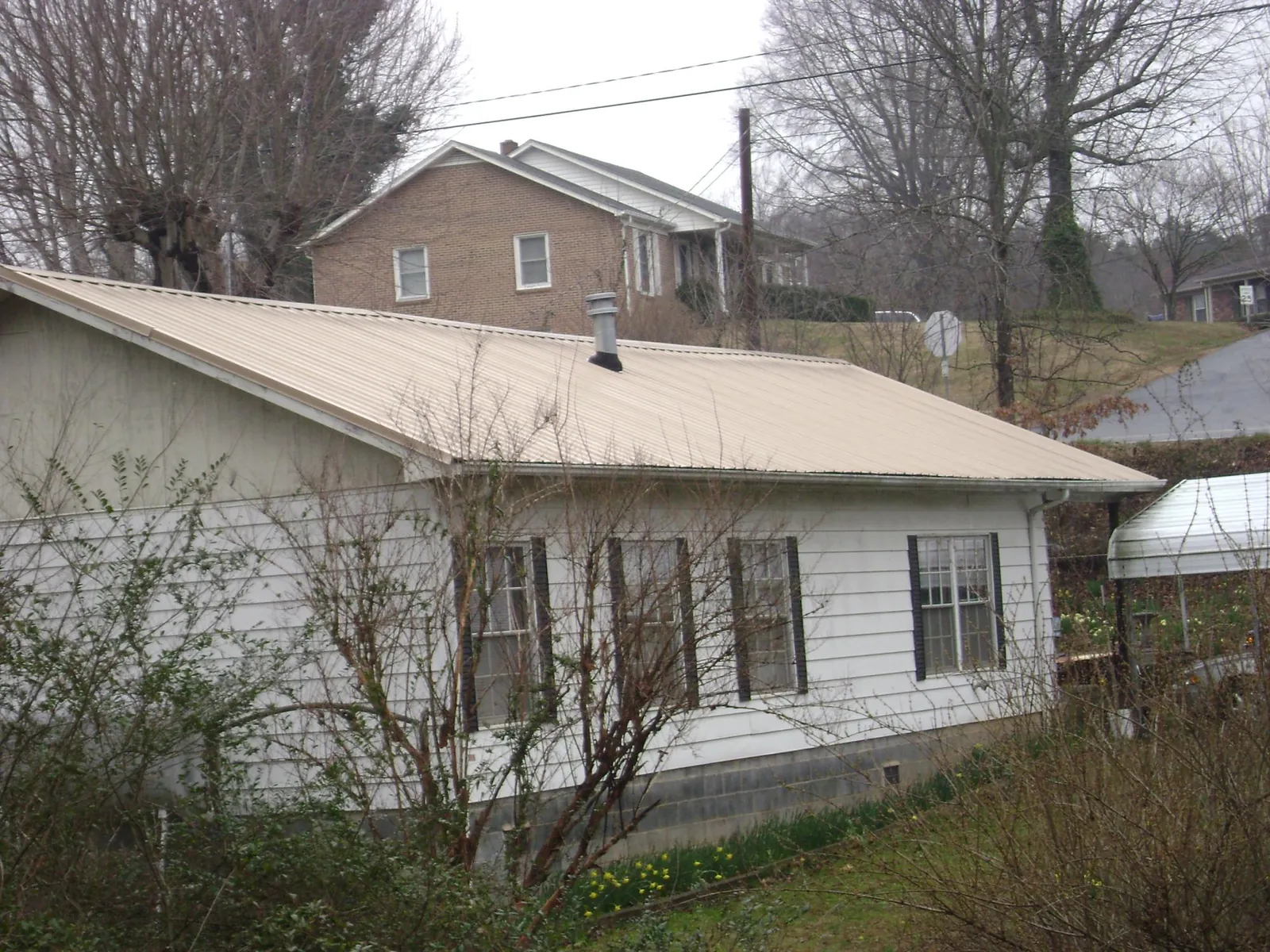 Tan metal roof on a white sided house set into a hillside — Commercial Roofing by Roofing Brothers in Nanticoke